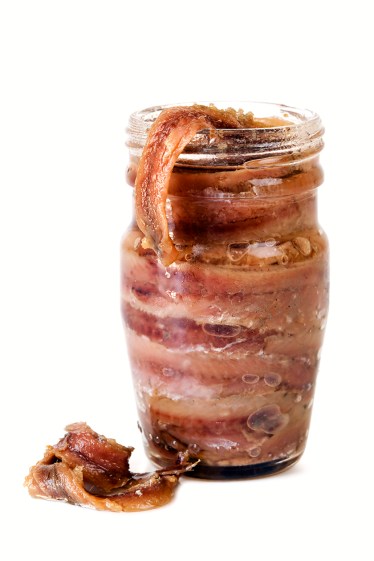 Open jar of anchovy fillets, isolated on white background.